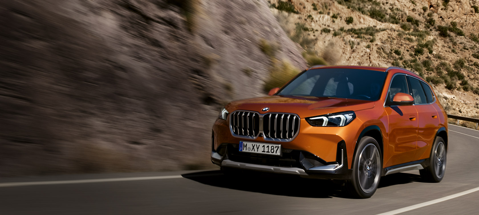 BMW X1 U11 xLine в цвете Utah orange metallic, вид спереди с поворотом в три четверти на грунтовой дороге